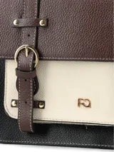 Cartera tipo satchel de diseño tricolor con solapa superior en marrón, cuerpo central en beige y base en negro. Presenta correas decorativas verticales con hebillas metálicas, manija superior rígida y correa larga ajustable y removible. Incluye logo metálico frontal y herrajes dorados.
