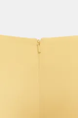 Top amarillo de manga corta abullonada, con cuello barco y bajo asimétrico. Cierre trasero con cremallera oculta.