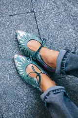 Zapato tipo blucher confeccionado en napa tornasolada con estampado de estrellas en color verde agua. Presenta un adorno artesanal de flecos en napa verde sobre el empeine, cierre con cordones, interior en piel y suela de cuero.