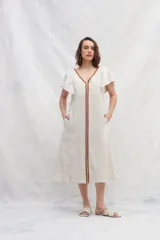 Vestido midi de lino en color crudo, con silueta amplia y escote en V tanto en el frente como en la espalda. Presenta mangas cortas con vuelo y detalles de cintas verticales en color marrón a contratono que recorren el frente. Incluye bolsillos laterales.