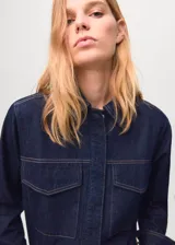 Camisa de jean de algodón con cuello camisero, cierre frontal de botones ocultos, mangas largas con puños abotonados y dos bolsillos delanteros con solapa.