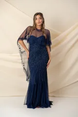 Vestido largo de fiesta color azul, confeccionado en tul bordado con diseño strapless. Incluye una capa tipo poncho de tul transparente con detalles bordados a juego, que cubre los hombros y cae hacia la espalda.