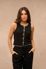 Top tejido de punto color negro, sin mangas, con cuello redondo y cierre frontal de botones. Presenta costuras y bordes con detalles en hilo crudo en contraste.