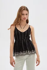 Blusa de algodón negra con tirantes finos regulables, escote en V y diseño holgado. Presenta detalles de bordado en color blanco verticalmente en el pecho y un delicado diseño floral bordado en el ruedo.