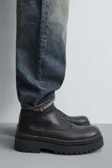 Bota de caña media con cierre frontal mediante cremallera, confeccionada en material con textura. Presenta una horma redonda y una suela de plataforma con diseño track.