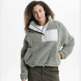 Campera de polar tipo sherpa color verde, con cuello alto y cierre frontal parcial con botones a presión. Presenta un bolsillo frontal con cierre y detalle de marca Reef.