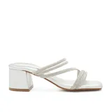 Sandalia de tacón cuadrado medio, color plateado, con tiras finas recubiertas de strass. Presenta puntera cuadrada y una pulsera ajustable al tobillo que puede retirarse para usar como chinela.