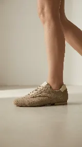 Zapato de estilo casual con diseño inspirado en championes, confeccionado en cuero gamuzado color beige. Presenta cordones al tono, costuras decorativas laterales y detalles en cuero liso en el talón y lengüeta.