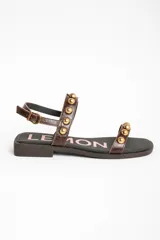 Sandalias planas de cuero marrón con tiras decoradas con tachas semiesféricas doradas, talón cerrado con tira ajustable y hebilla metálica.