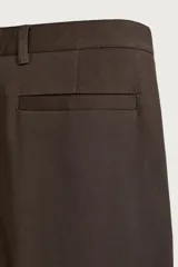 Pantalón chino de corte regular, color marrón oscuro, con cierre frontal de cremallera y botón, bolsillos laterales y bolsillos traseros de vivo.