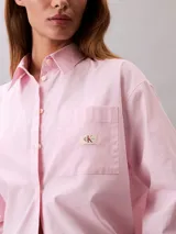 Camisa de corte relaxed confeccionada en popelina de algodón con elastano. Presenta cuello de punta clásico, cierre frontal con botones, mangas largas y un bolsillo en el pecho con el monograma CK bordado en relieve.