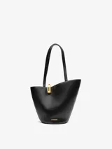 Bolso tipo tote asimétrico de cuero liso color negro, con diseño de cubo, doble asa superior y cierre de anilla metálica dorada. Incluye logo de la marca en letras doradas en la parte inferior.