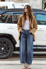 Jeans de tiro alto con diseño barrel, confeccionados en denim azul. Presentan cinco bolsillos, cierre frontal con botones y detalle de costuras verticales en el frente y la espalda. Su corte es holgado en la pernera y se estrecha hacia el tobillo.