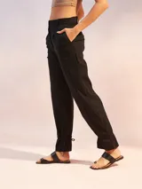 Pantalón de tiro alto color negro, confeccionado en mezcla de lino. Presenta corte recto con pinzas en la cintura, bolsillos laterales y un detalle de ajuste con lazo en los tobillos que crea un efecto acampanado.