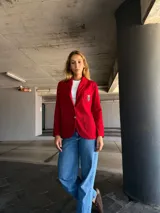 Blazer rojo con solapas, cierre con un botón dorado y escudo bordado en el bolsillo.
