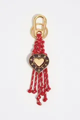Llavero con mosquetón dorado, cuerpo de cuerdas entrelazadas rojas con detalles blancos, y dije central en forma de corazón esmaltado en color marrón con letras doradas y un corazón metálico dorado en el centro.