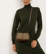 Cartera pequeña de diseño transversal con estructura rígida, confeccionada en una combinación de cuero sintético y sarga de algodón. Presenta una solapa frontal con detalle de hebilla decorativa y costuras a la vista, acompañada de una correa larga ajustable para llevar al hombro o cruzada.