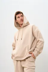 Buzo canguro beige de corte holgado con capucha y cordones ajustables.