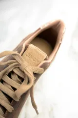 Zapatillas bajas de cuero color marrón con estrella beige en el lateral, cordones color beige y detalle dorado en el talón.