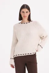 Sweater de punto grueso en color beige, con diseño de cuello redondo y detalle de pespuntes decorativos en color chocolate en el cuello, el ruedo y los puños.