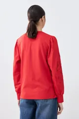 Sweatshirt de algodón color rojo, con cuello redondo y mangas largas abullonadas que presentan detalles de calados bordados. Posee puños elásticos y un diseño holgado.
