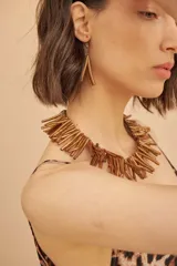 Collar de diseño llamativo confeccionado con múltiples tubos alargados de tono dorado envejecido, dispuestos en forma de flecos alrededor del cuello.