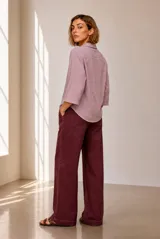 Blusa azul de lino con cuello camisero, escote en V y mangas tres cuartos con vuelta. Presenta un diseño holgado con dobladillo redondeado y un pequeño parche con logo bordado en el lateral inferior.