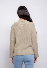 Sweater color crema de tejido trenzado con cuello alto, mangas largas abullonadas y detalle de flecos en el frente.