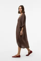 Vestido midi de lino color marrón, de corte amplio y silueta asimétrica con escote en V y detalle fruncido en el centro del frente. Presenta mangas cortas holgadas con vuelta y diseño relajado.