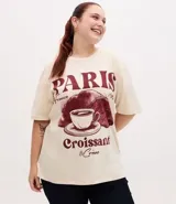 Remera de algodón color crema con cuello redondo y mangas cortas. Presenta un estampado frontal con temática parisina que incluye la palabra 'Paris', un dibujo de una taza de café sobre un croissant y la frase 'Croissant & Crème'.
