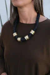 Collar de diseño artesanal compuesto por múltiples hilos de cordón negro entrelazados, intercalados con piezas cilíndricas de metal dorado con textura irregular y acabado rústico.