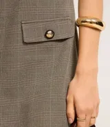 Vestido corto sin mangas confeccionado en crepé con estampado de cuadros. Presenta escote en V tanto en la parte delantera como en la trasera, breteles anchos y lapelas delanteras con botones estilizados.