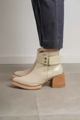 Bota corta de cuero negro con acabado combinado mate y charol. Presenta una tira decorativa con tachas metálicas y hebilla en el tobillo, tacón cuadrado robusto y suela con plataforma.