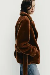 Chaqueta de textura efecto pelo en color marrón, con cuello de solapa, manga larga y cierre frontal cruzado mediante cinturón del mismo tejido. Cuenta con bolsillos delanteros.
