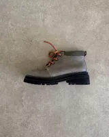 Borcego de cuero color gris con cordones color naranja, suela track negra de goma y detalle de gamuza en la parte superior del tobillo.