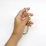 Collar de cuentas redondas de serpentina en tonos de verde claro y blanco, ensartadas con hilo verde y terminaciones y broche tipo anilla de acero con baño de oro.