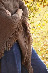 Poncho tejido en lana merino color marrón, con diseño de punto acanalado y terminación con flecos en el borde inferior. Incluye una pequeña etiqueta de cuero en la parte posterior.