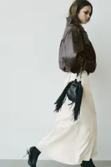 Bolso tipo saca color negro, de formato mini, con flecos laterales, cierre fruncido con cordones y correa combinada de cadena y tira de cuero sintético.