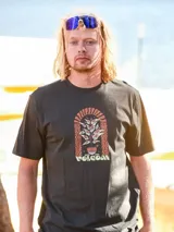 Remera Volcom de manga corta y cuello redondo en color negro, con estampado gráfico central que representa una planta con hojas en forma de ojos dentro de un arco decorativo y el logotipo de la marca.