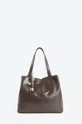 Cartera tipo tote de color marrón con acabado brillante, doble asa de hombro y detalle de colgante con cuentas de colores en uno de los laterales.