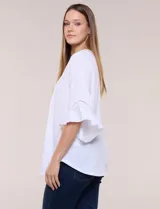 Blusa blanca de crepe crinkle con escote en V, media abotonadura frontal con botones nacarados, alforzas verticales en la pechera y mangas tres cuartos acampanadas con detalle de encaje horizontal.