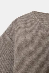 Chaqueta corta de punto color beige, con cuello redondo y manga tres cuartos. Cierre frontal con tres botones forrados a tono.