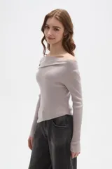 Sweater de punto acanalado color gris claro, con diseño de hombros descubiertos y cuello asimétrico drapeado. Presenta mangas largas y un corte ajustado al cuerpo.