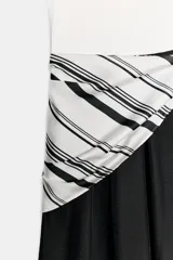 Vestido midi bicolor con parte superior blanca tipo musculosa con ribetes negros y falda negra evasé. Cuenta con un detalle de pañuelo a rayas en blanco y negro anudado en la cintura, bolsillos laterales y cierre con cremallera.