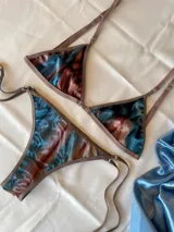 Conjunto de bikini confeccionado en terciopelo con efecto degradado en tonos azul, marrón y rosado. El corpiño es de estilo triangular con aros metálicos decorativos en el centro y breteles regulables. La bombacha es de corte clásico con laterales ajustables mediante tiras.