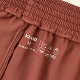 Short deportivo de secado rápido, con diseño de doble capa en color marrón y rosa. Presenta cintura elástica con cordón ajustable y logo estampado en el frente.