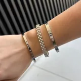 Set de tres pulseras de acero quirúrgico en tono plateado. Incluye dos esclavas rígidas con detalles de flores y piedras incrustadas, y una pulsera de eslabones tipo reloj.