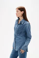 Camisa de jean negro con diseño de frunces verticales en el frente, cuello clásico, cierre frontal con botones y mangas largas con puños abotonados.