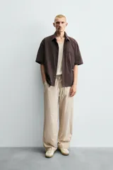 Pantalón relaxed fit color beige con rayas verticales finas, confeccionado en tejido de algodón. Cuenta con cintura elástica ajustable con cordón, bolsillos frontales y bolsillos traseros de plastrón.