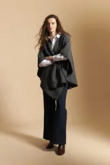 Poncho de tejido suave color beige con diseño envolvente y terminaciones con costuras decorativas en contraste color negro. Presenta un detalle de lazo frontal integrado.